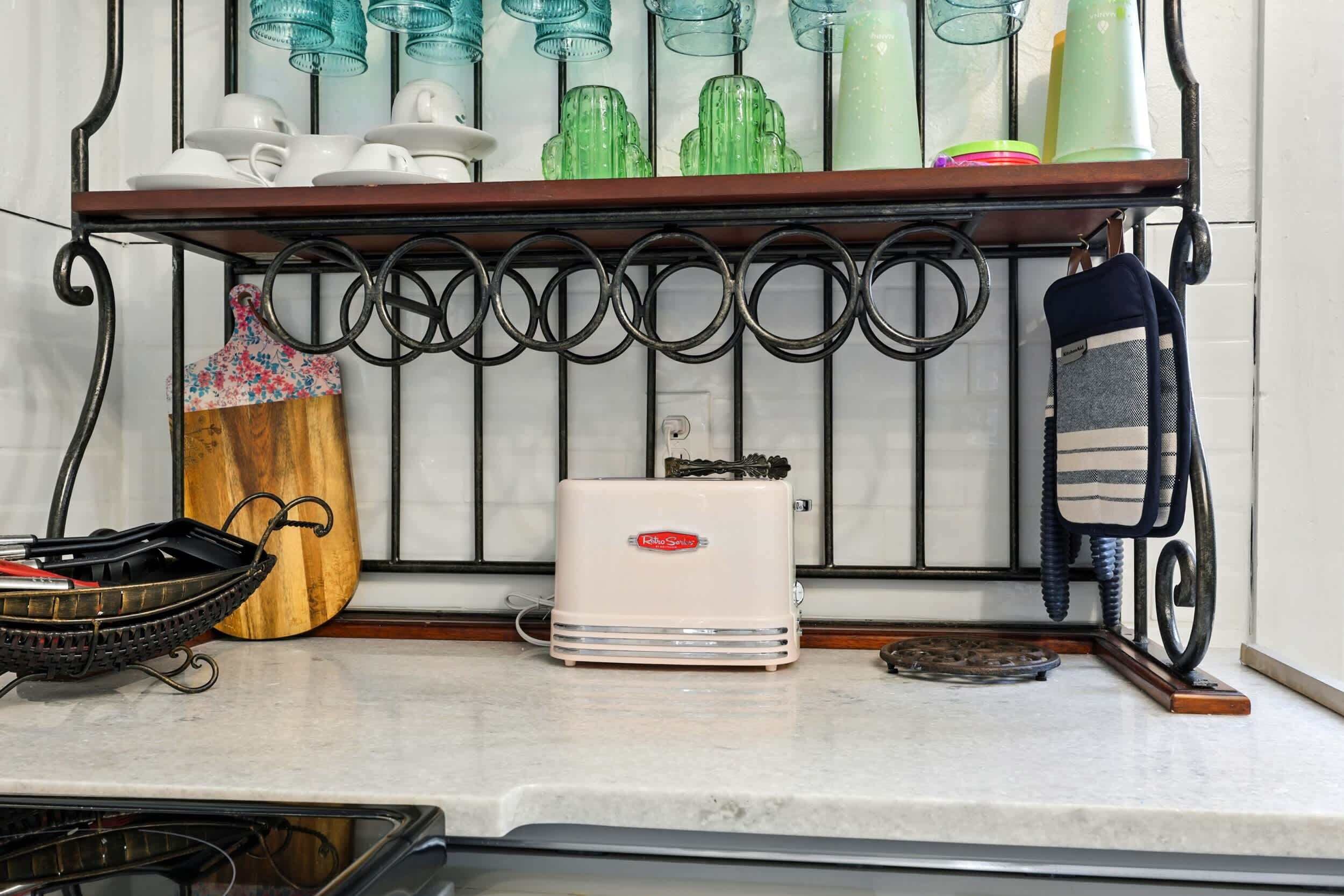 Un comptoir de cuisine avec une machine à café, un panier et un étendoir suspendu où sont rangées des tasses et des verres.