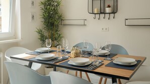 A dining area with a wooden table set for four, surrounded by chairs, with a large plant and a wall-mounted shelf with candles.