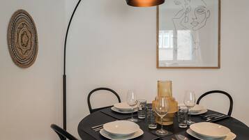 Mesa de jantar posta com pratos, copos e talheres, uma luminária e uma obra de arte na parede.