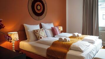 A neatly made bed with white linens and a brown throw blanket, a wall-mounted decorative item, and a window with curtains.