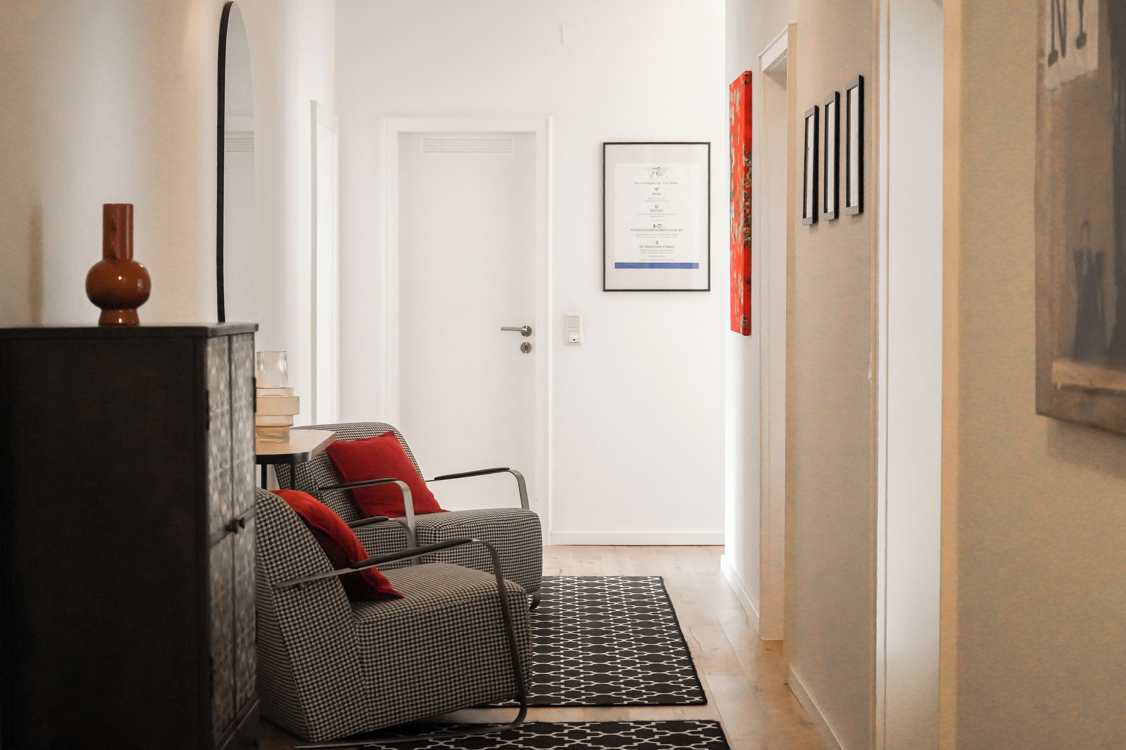 Een hal met een gestreept bankje, een patroonrijk vloerkleed en een ingelijst certificaat aan de muur.