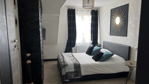 Un dormitorio moderno con una cama grande, una mesita de noche, una lámpara colgante y un ventanal con cortinas.