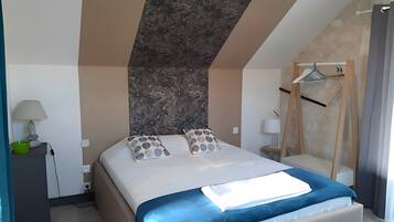 A hotel room with a bed, pillows, a lamp, a bowl, a hanging rack, and a wall with a textured pattern.