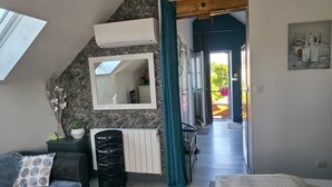 Un dormitorio con tragaluz, radiador, espejo, cama, silla, una mesita y vistas al exterior.