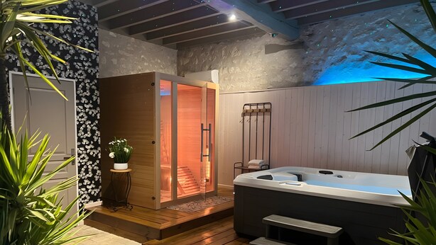 Un área de spa con un jacuzzi, escalones de madera, una planta en maceta y una pared con textura.