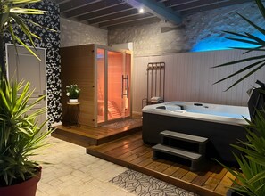 A spa area with a hot tub, wooden steps, a potted plant, and a wall with a textured pattern. - Holiday Home 'Des Caves' with Shared Pool, Wi-Fi and Air Conditioning (Sainte-Maure de Touraine)