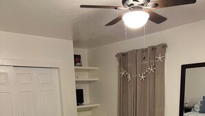 Ein Schlafzimmer mit Bett, Deckenventilator, Kleiderschrank, Schreibtisch und einem Fenster mit Vorhängen.