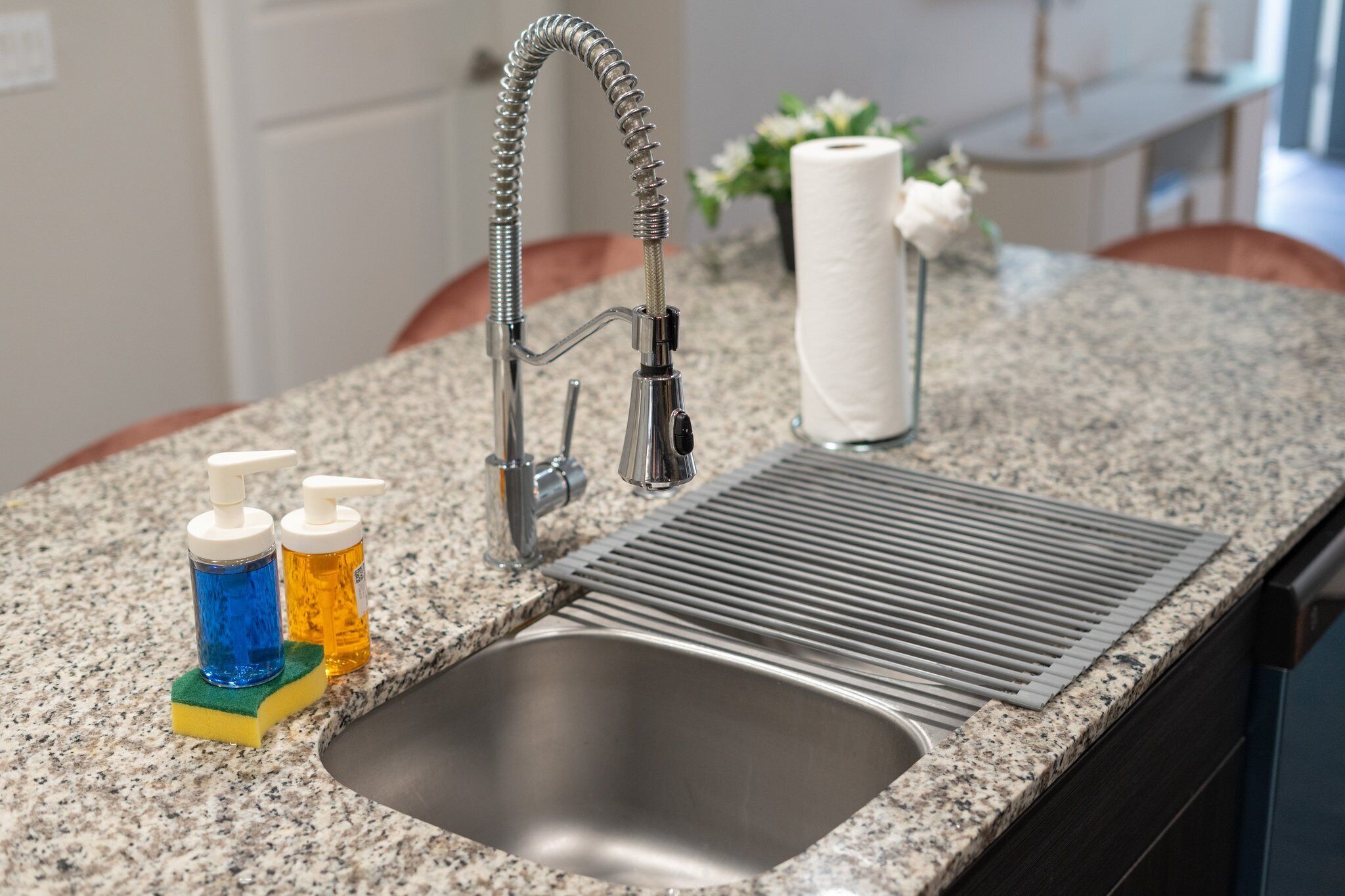 A kitchen sink with a modern faucet, a built-in strainer, and two soap dispensers on a granite countertop.