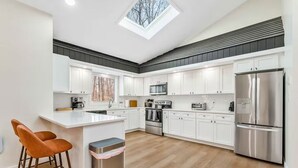 A modern kitchen with white cabinets, stainless steel appliances, and a skylight.