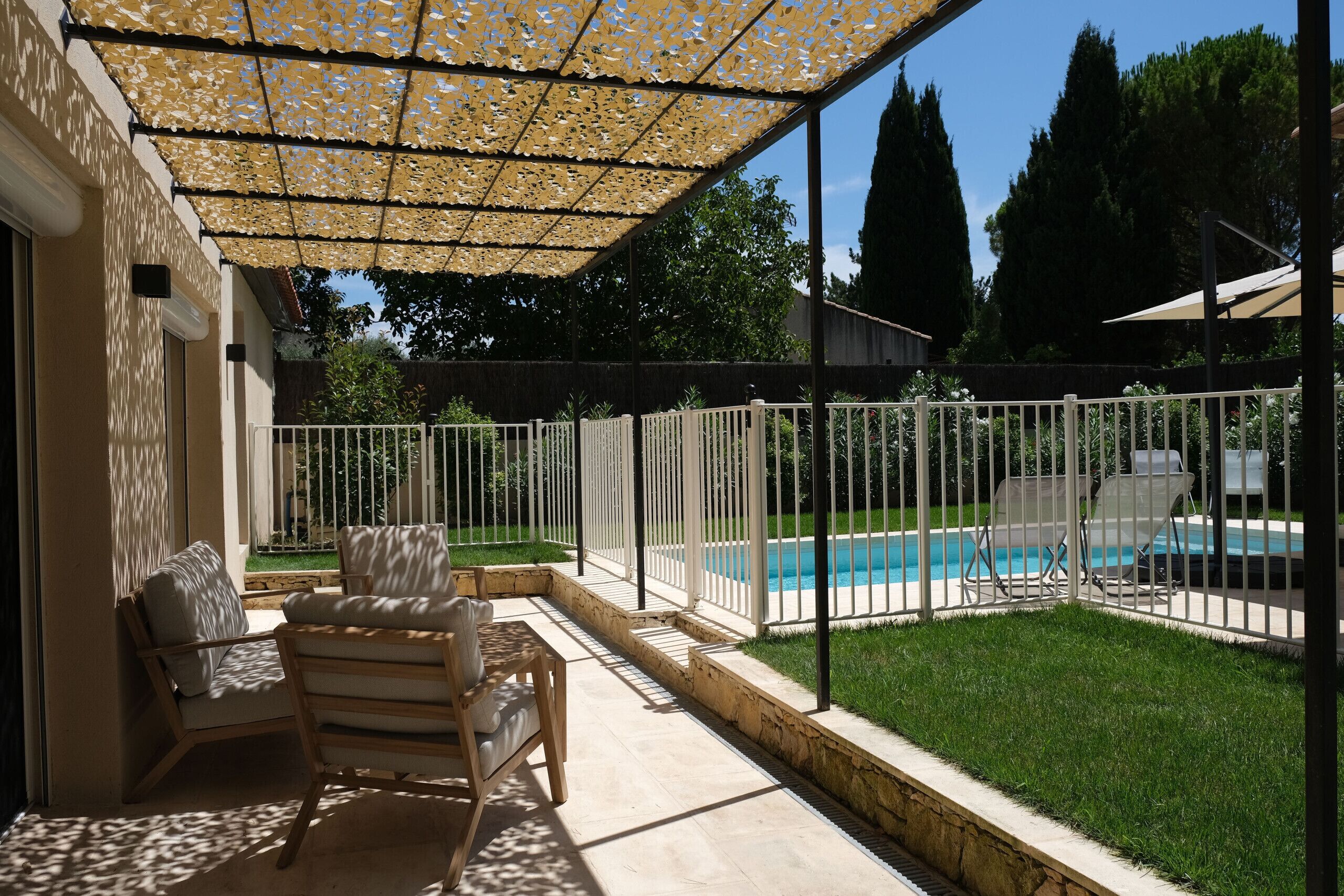 Un patio techado con piscina, mobiliario exterior y cerca blanca.