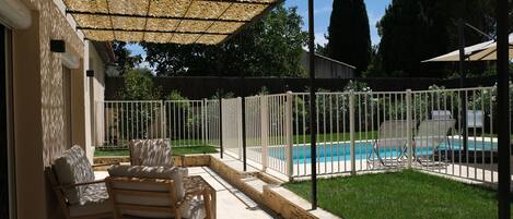 Un patio techado con piscina, mobiliario exterior y cerca blanca.