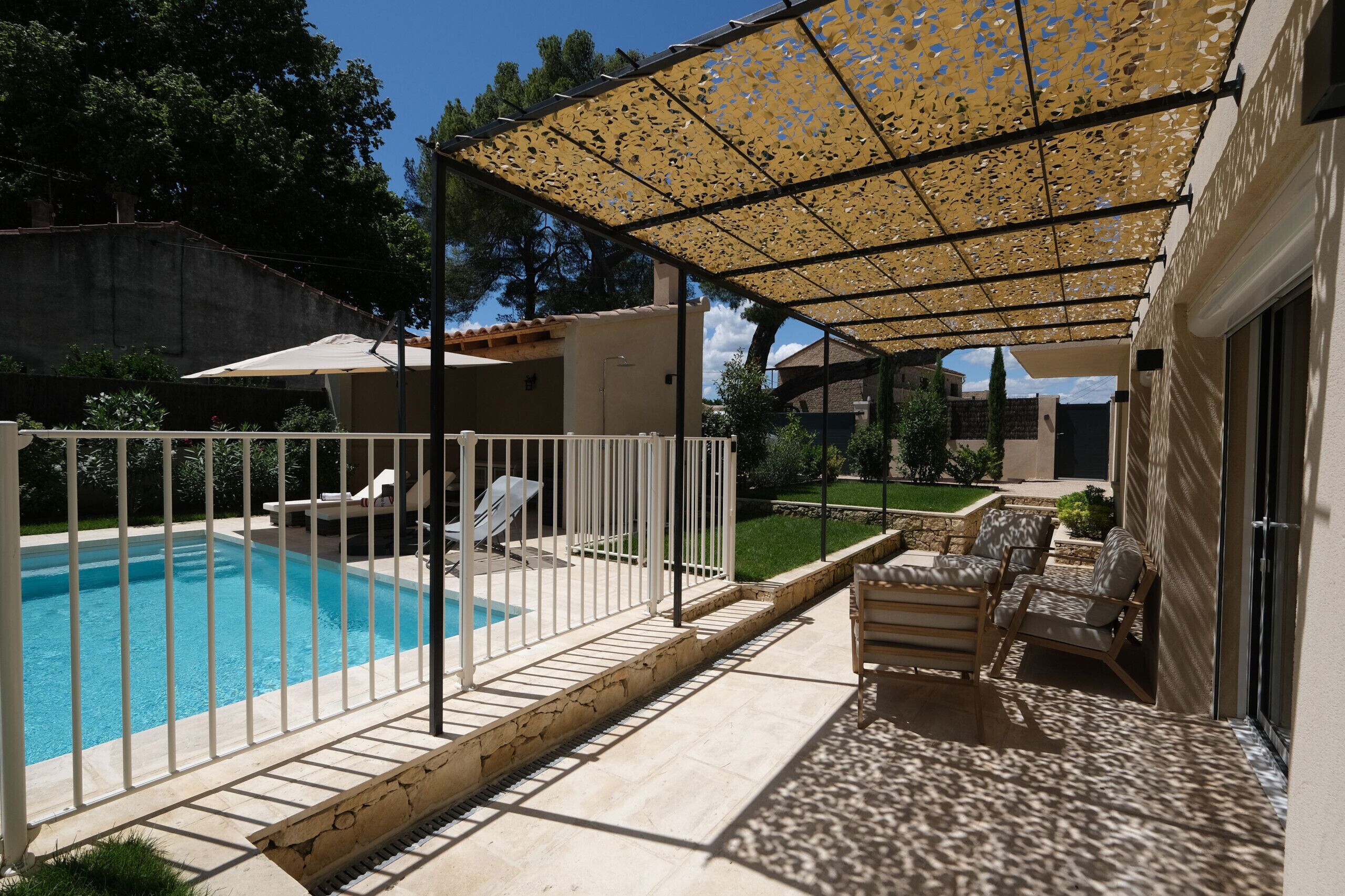 A pool area with a covered patio, lounge chairs, and a white fence.