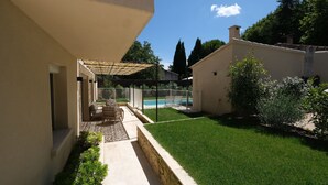 Un patio con piscina, una zona de estar techada y un césped bien cuidado.