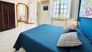 Une chambre avec un grand lit, deux coussins à motifs, une fenêtre donnant sur un beau paysage, un radiateur et une armoire en bois.