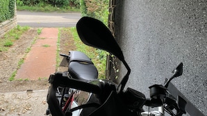 Een motorfiets geparkeerd naast een gebouw, met een verhard pad dat naar een weg leidt.