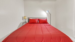 Una cama con una colcha roja y dos almohadas rojas en una habitación con paredes blancas y techo inclinado.