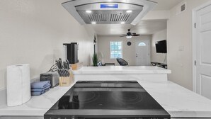 Una cocina moderna con una placa de inducción negra, una campana extractora de acero inoxidable y una encimera de mármol blanco.