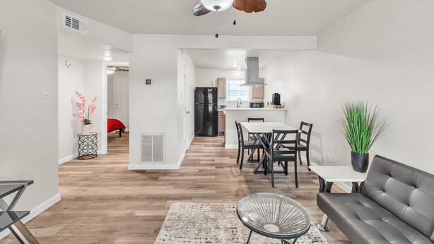 Una sala de estar moderna con ventilador de techo, un comedor con mesa y sillas, y una cocina al fondo.