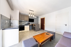 A modern kitchen with a dining area, a sofa, and a television.