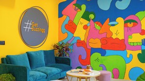 Un'accogliente stanza con un divano color petrolio, un tavolino rotondo e un murale astratto dai colori vivaci sulla parete.