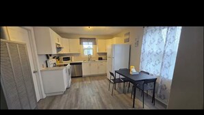 A compact kitchen with white cabinets, a microwave, and a dining area with a table and chairs. - Cozy 2-Bedroom Apartment (Cornwall)