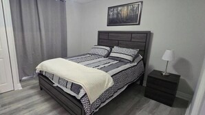 A bedroom with a bed, a nightstand, a door, and a painting on the wall. - Cozy 2-Bedroom Apartment (Cornwall)