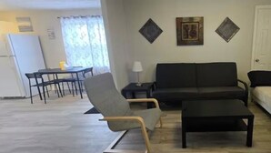 A living room with a sofa, armchair, and coffee table. There is a dining area with a table and chairs. - Cozy 2-Bedroom Apartment (Cornwall)