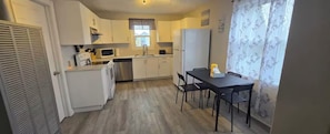 A compact kitchen with white cabinets, a microwave, and a dining area with a table and chairs.