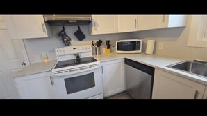A compact kitchen with white cabinets, a stove, a microwave, and a dishwasher. - Cozy 2-Bedroom Apartment (Cornwall)