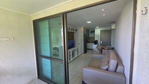 A modern apartment with a sliding glass door leading to a balcony, a living area with a sofa, a kitchen with a dining table, and a refrigerator. - Beach Class Resort 1305 by La Playa  (Ipojuca)