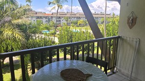 A balcony with a covered table and chairs, a view of a pool and buildings, and a tropical landscape. - Beach Class Resort 1305 by La Playa  (Ipojuca)