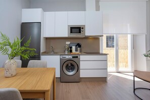 Cocina compacta con lavadora, microondas y comedor con mesa y sillas.