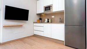 A modern kitchen with white cabinets, a built-in microwave, a stainless steel refrigerator, and a flat-screen TV mounted on the wall. - Genteel Home Trinidad Grund B (Málaga)