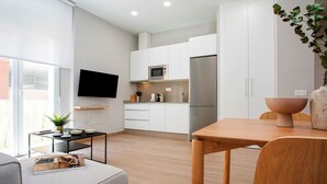 A modern kitchen with white cabinetry, a stainless steel refrigerator, a microwave, and a flat-screen TV. - Genteel Home Trinidad Grund B (Málaga)