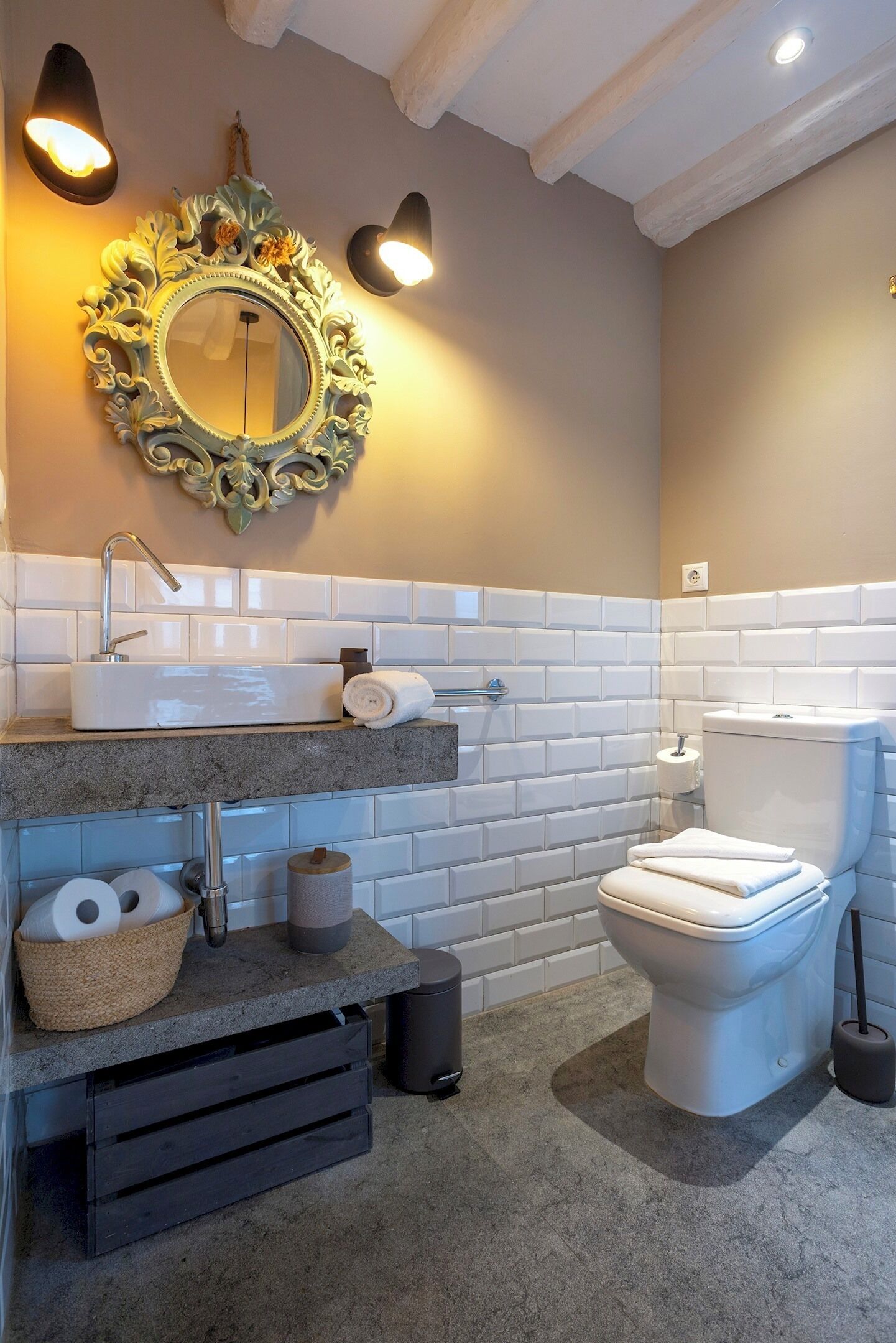 Un baño con lavamanos blanco, inodoro y un espejo decorativo con apliques de pared.