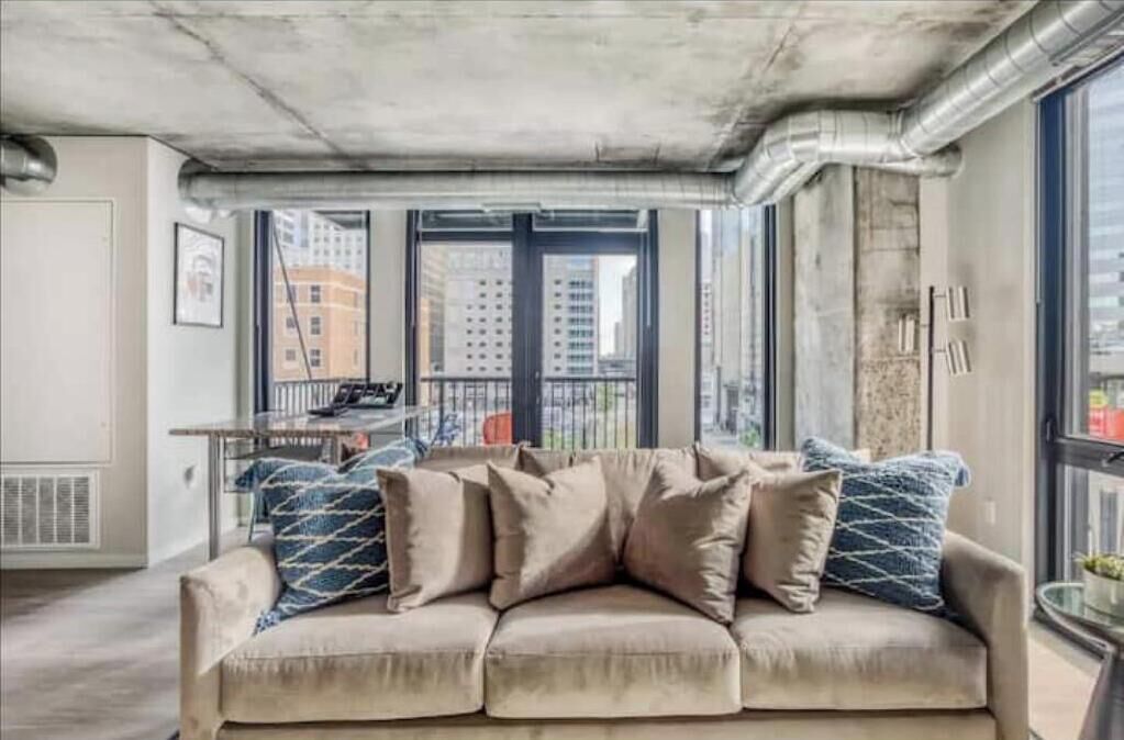 Ein modernes Wohnzimmer mit einem beigefarbenen Ecksofa, großen Fenstern und Blick auf die Stadt.