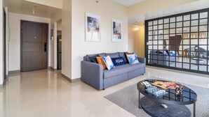 A modern living room with a grey sofa, a coffee table, and a large window with a view of the outside. - Bayshore  Captain Quarters 50% Off| Bayview & Pool (Parañaque)
