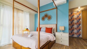 A bedroom with a four-poster bed, a bedside table with a lamp, and a wall with decorative art. - Bayshore  Captain Quarters 50% Off| Bayview & Pool (Parañaque)