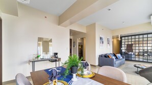 A modern living room with a sofa, a dining table set with gold and white tableware, and a potted plant. - Bayshore  Captain Quarters 50% Off| Bayview & Pool (Parañaque)
