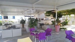 Un espace extérieur aménagé avec des canapés en osier, des chaises violettes et jaunes, et des plantes en pot.