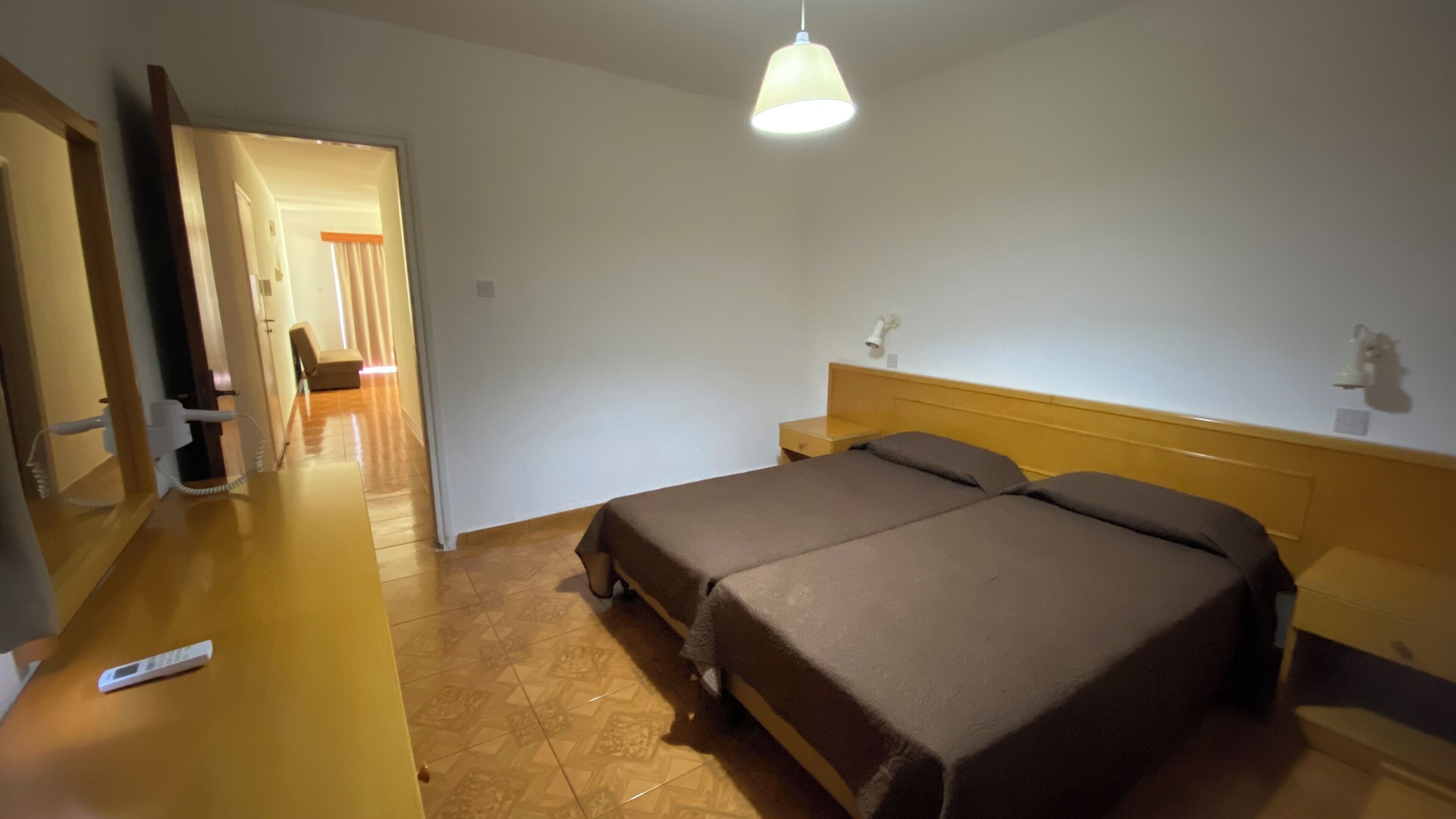 Een slaapkamer met een bed, nachtkastje, lamp en een deur naar een andere kamer.