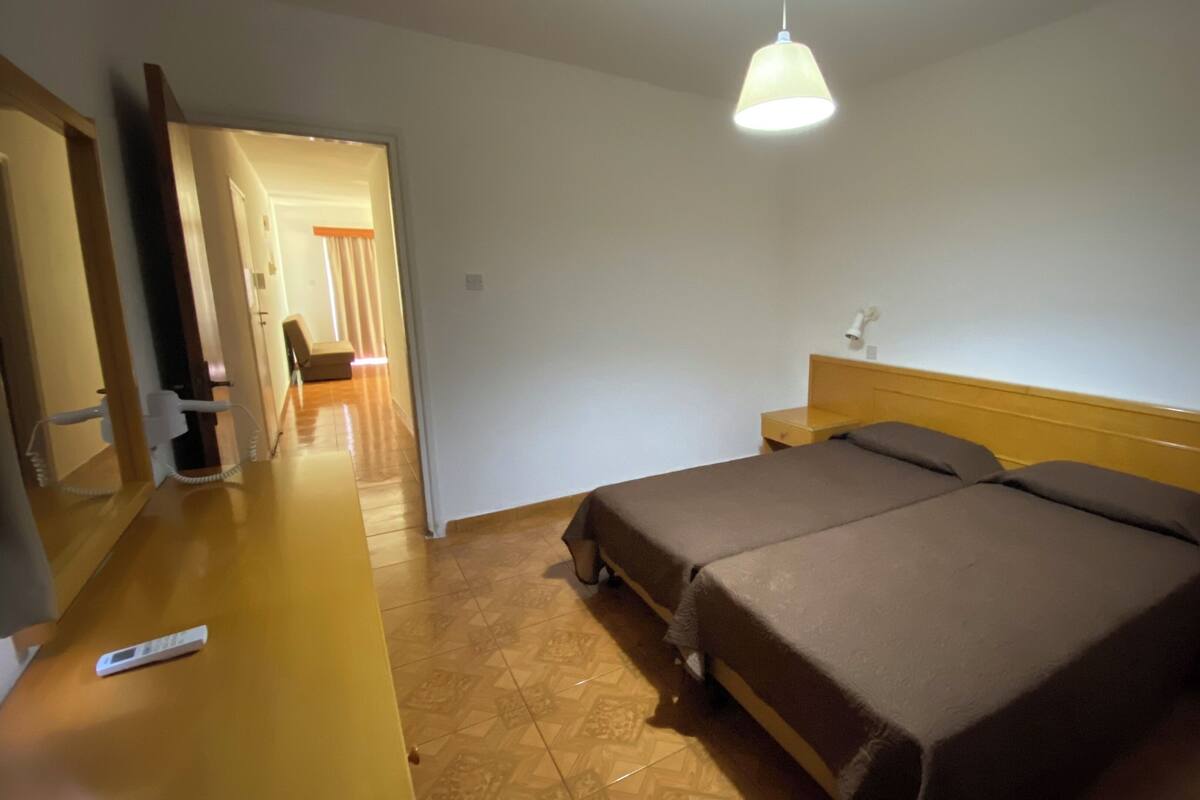 Ein Schlafzimmer mit Bett, Nachttisch, Lampe und einer Tür zu einem anderen Raum.