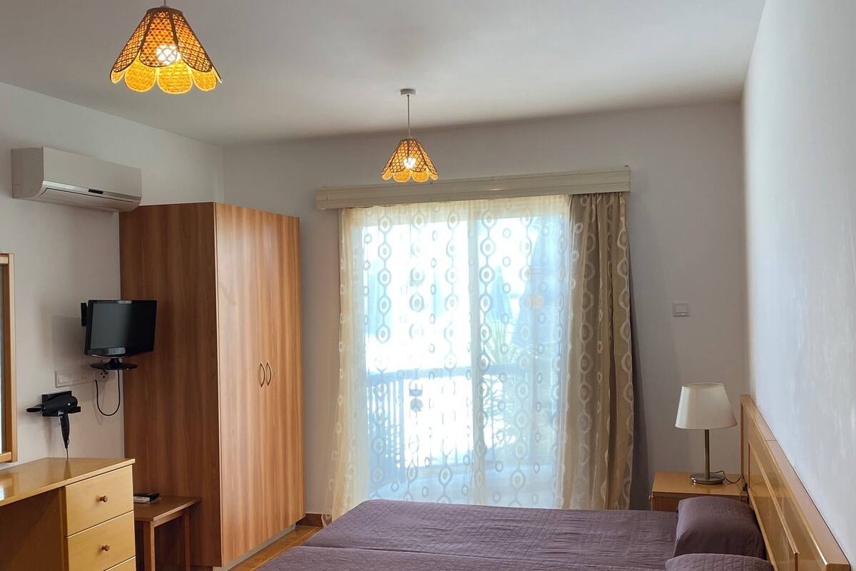 Ein Schlafzimmer mit einem Bett, einem Schreibtisch, einem Fernseher und einem Fenster mit Vorhängen.