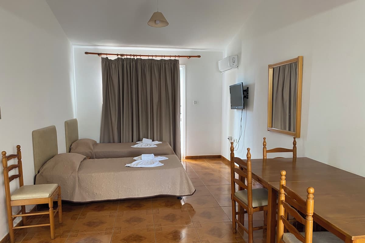 A room with two beds, a wooden dining table, chairs, a TV, and a window with curtains.