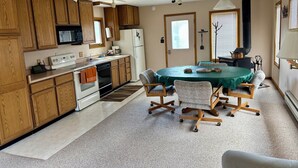 A compact kitchen with wooden cabinets, a microwave, a stove, and a refrigerator. There's a dining table with chairs and a ceiling fan.
