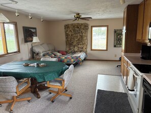A compact living space with a kitchenette, a dining area with a table and chairs, a sofa, a stone wall, and a ceiling fan.