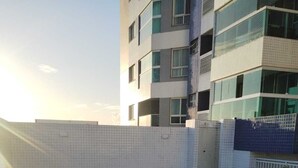 En swimmingpool med flisebelagt område og metalgelændere, omgivet af en hvid mur og en bygning med flere vinduer og balkoner.