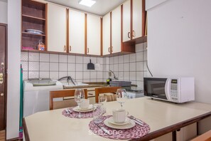 A kitchen with wooden cabinets, a microwave, a sink, and a dining table set with plates, glasses, and cutlery. - Apto bem Localizado a 500mts da Praia Rhi206 (Florianópolis)