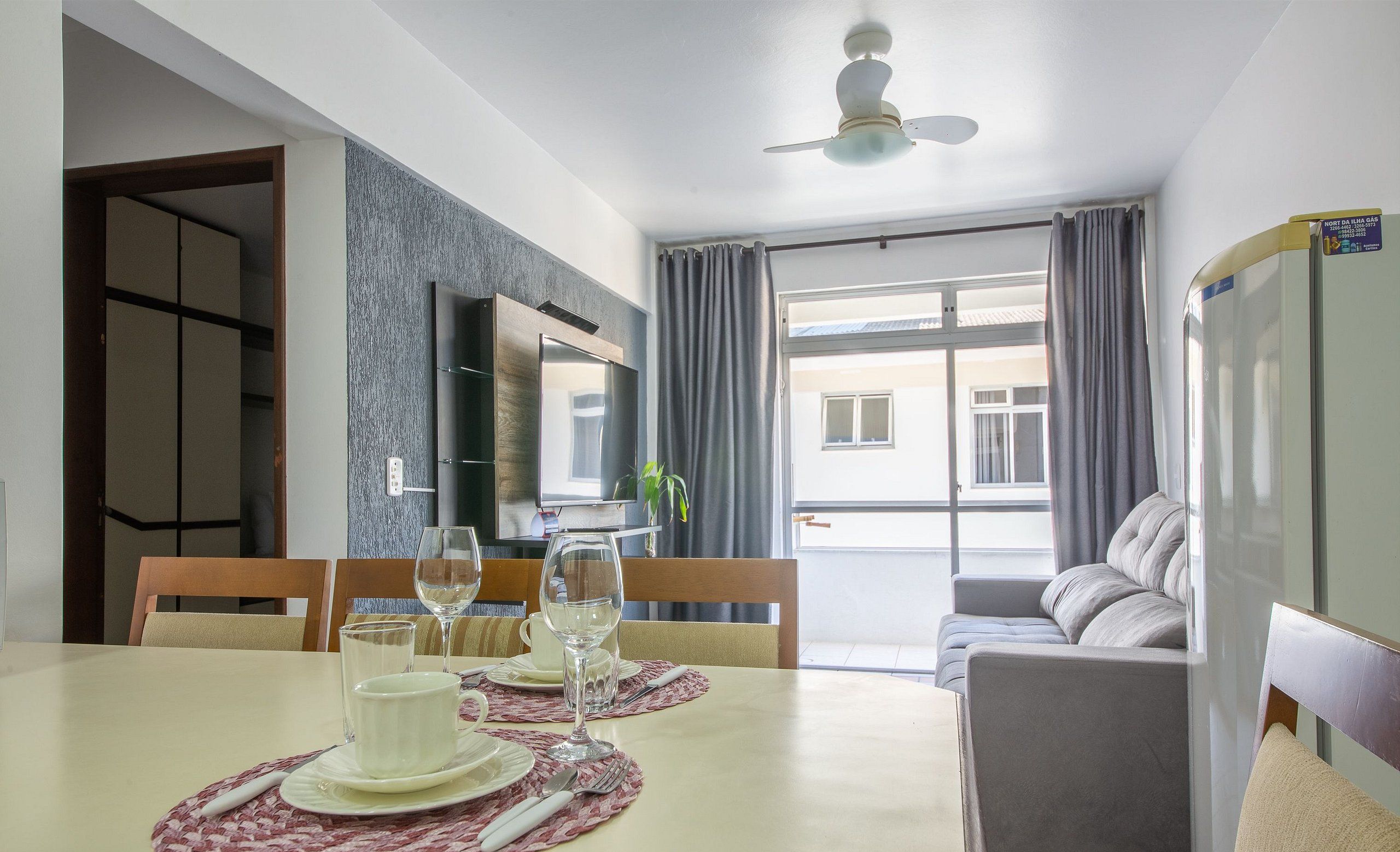 A dining area with a table set for two, a sofa, and a TV.