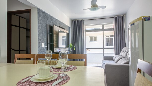 A dining area with a table set for two, a sofa, and a TV. - Apto bem Localizado a 500mts da Praia Rhi206 (Florianópolis)